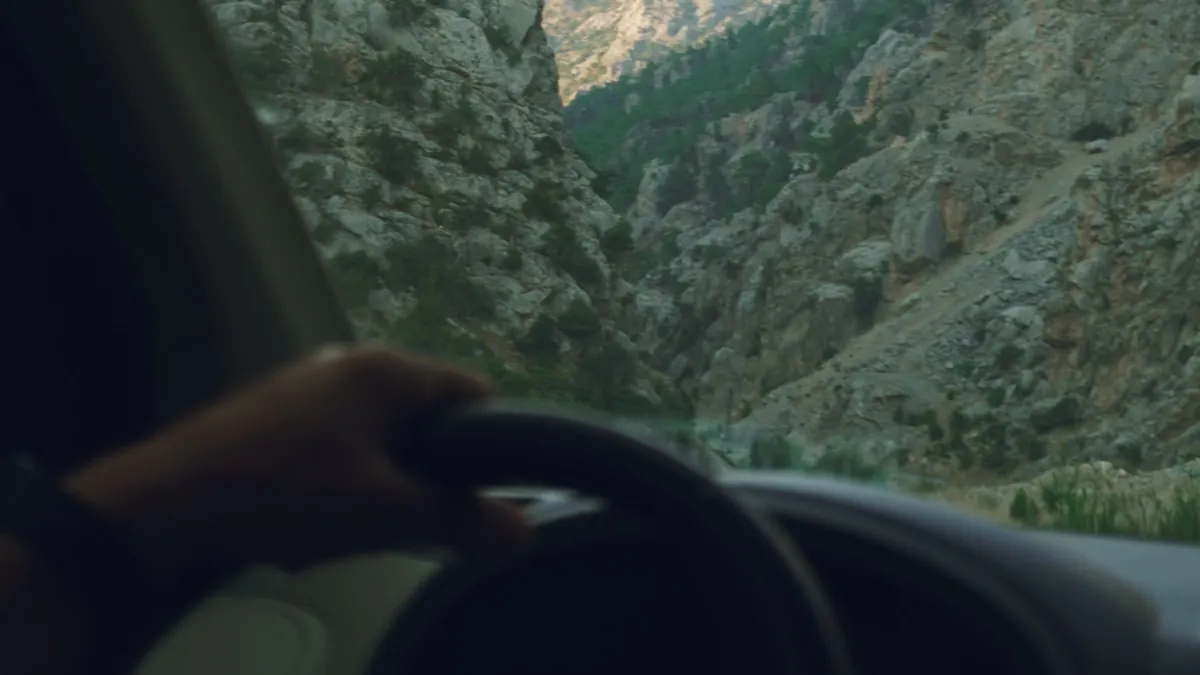 Eine Hand am Lenkrad eines Autos, das durch ein Bergtal fährt