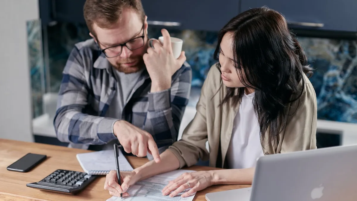 A couple at a kitchen table filling in a form, with a calculator and a laptop